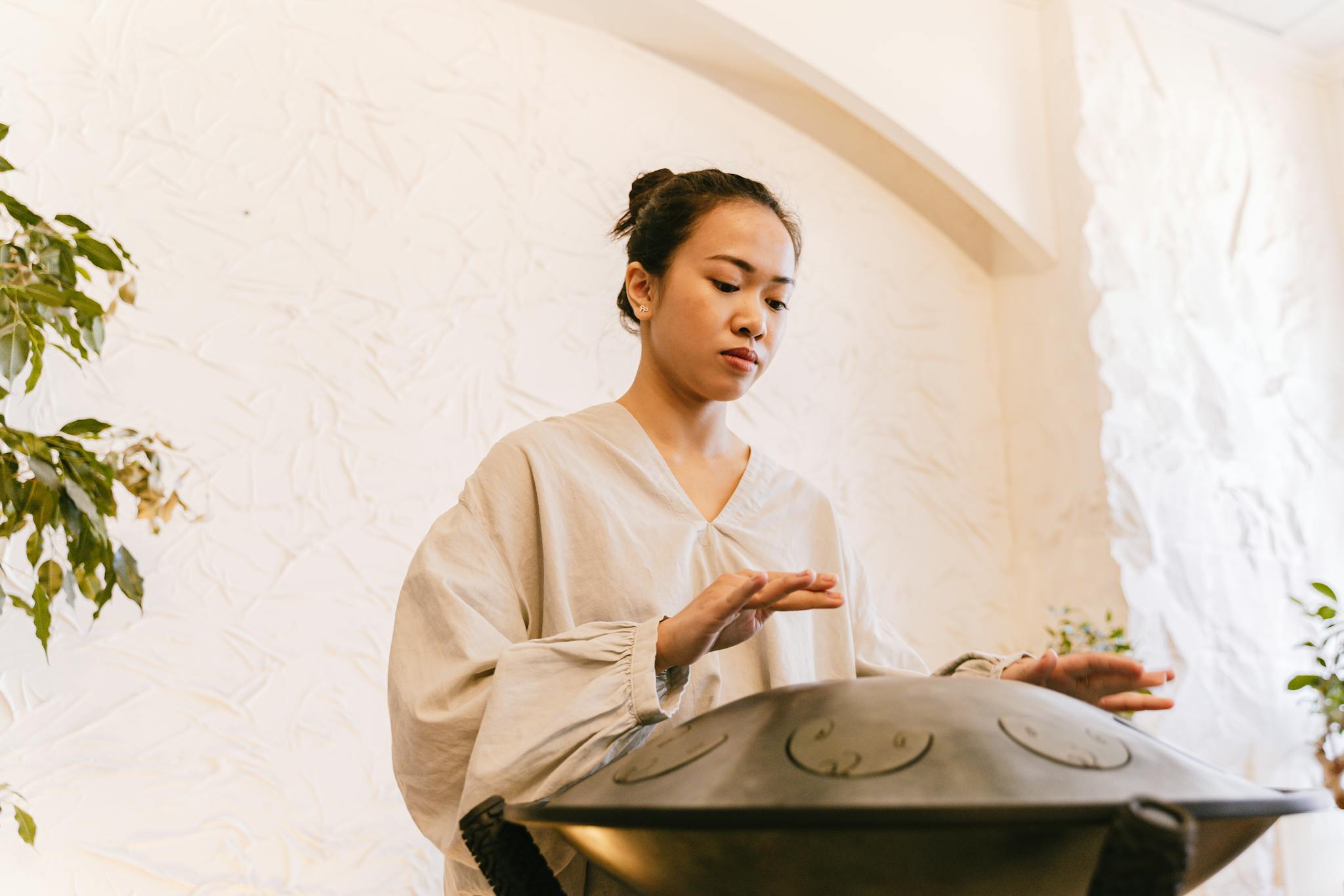Asian woman using handpan for alternative therapy and relaxation indoors.