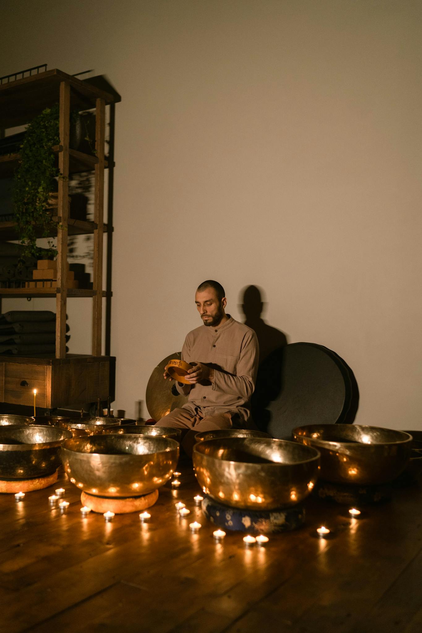 Man meditating with Tibetan singing bowls and candles, creating a serene atmosphere indoors.